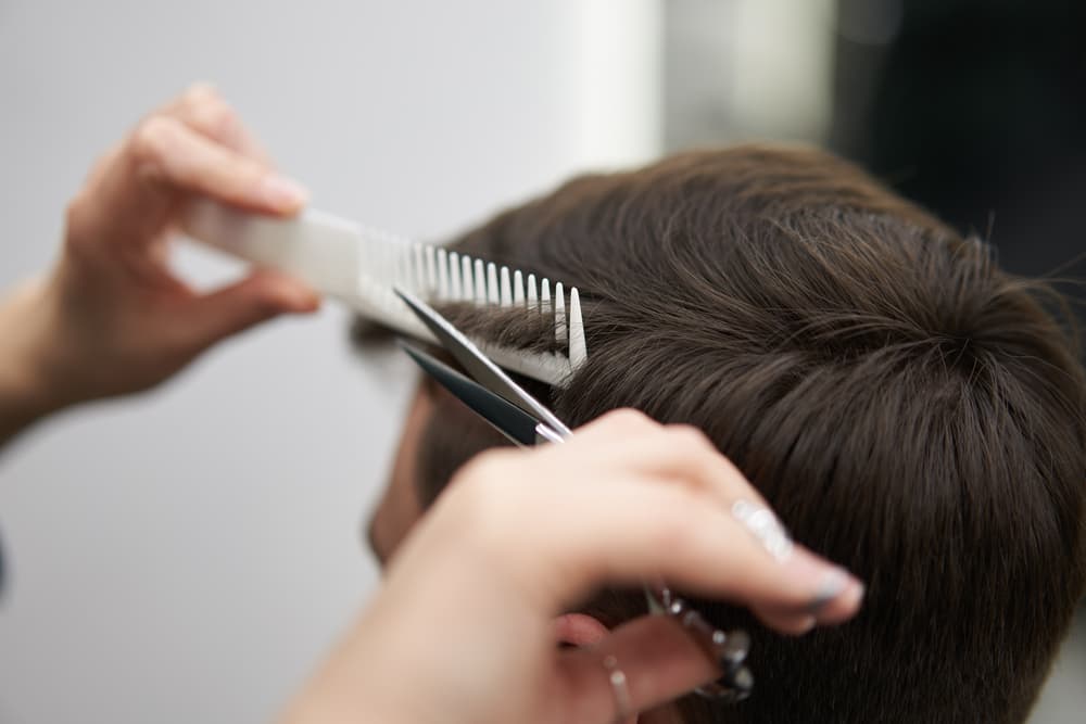 Close-up of a stylist cutting a man’s hair with scissors and comb, showing professional gents haircutting at The Classic Hair Company in Tilbury.