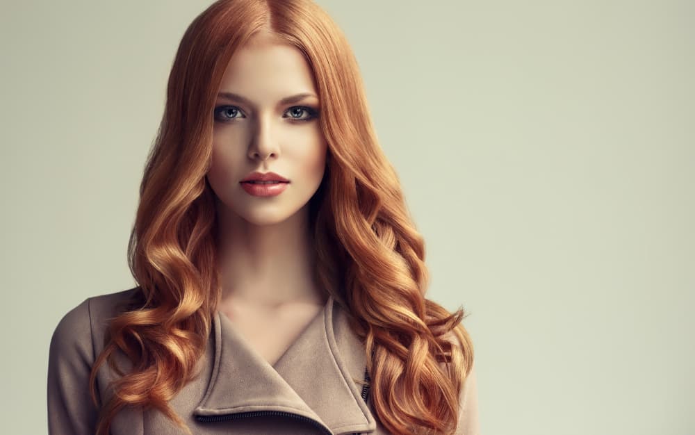 Stylish woman with long, glossy red hair and soft curls, showcasing professional hair colouring at The Classic Hair Company in Tilbury.