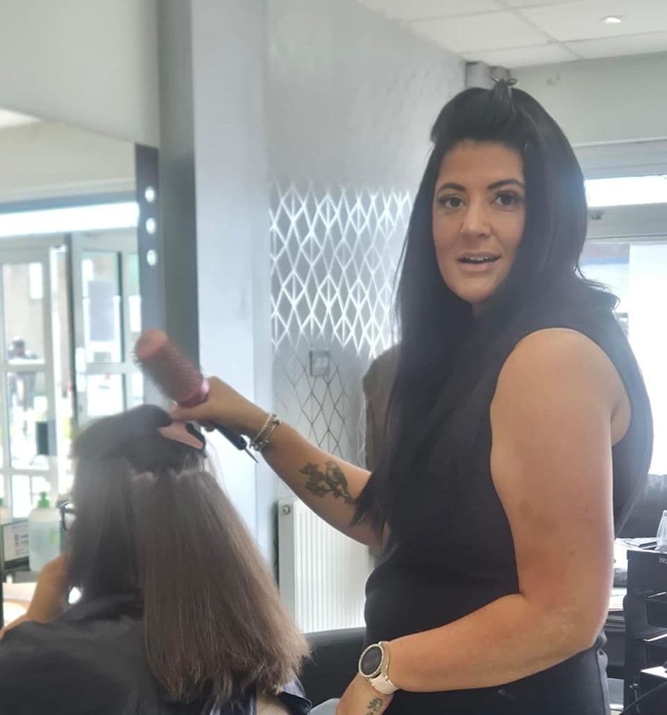 Hannah Bibby, Advanced Stylist at The Classic Hair Company in Tilbury, Essex, smiling while answering the phone at the salon reception desk.